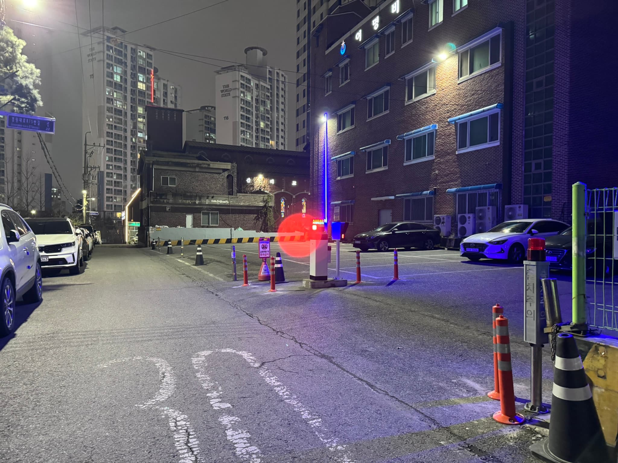 도로 한쪽에서 바라본 접근 구간. 도로 가장자리의 주차 차량과 바로 맞닿은 출입구 때문에 차량이 짧은 구간에서 방향을 틀어 진입해야 합니다.